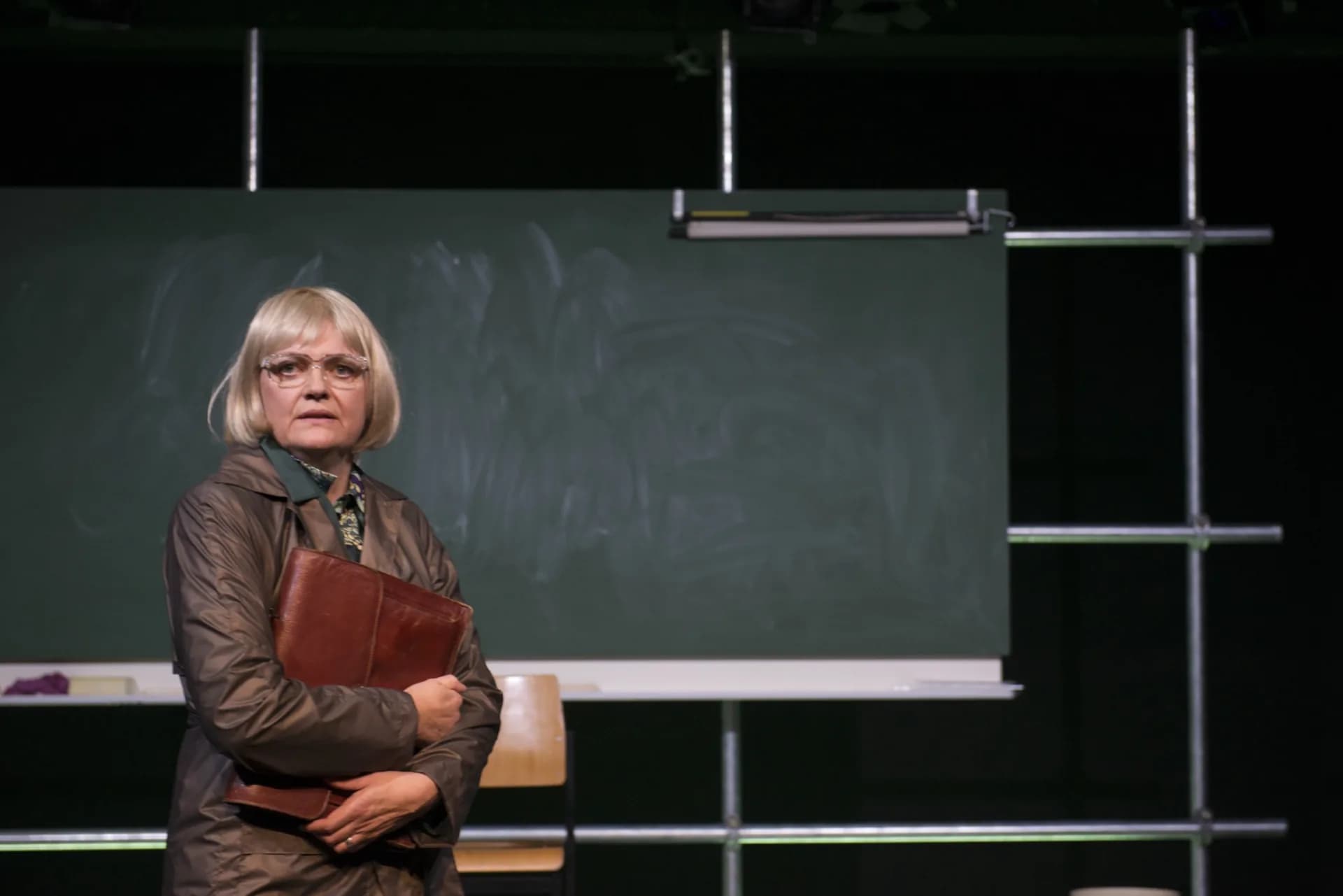 Anna Windmüller in einer Bühnenszene vor einer Schultafel, nachdenklich mit Mappe in der Hand — fragender, suchender Ausdruck