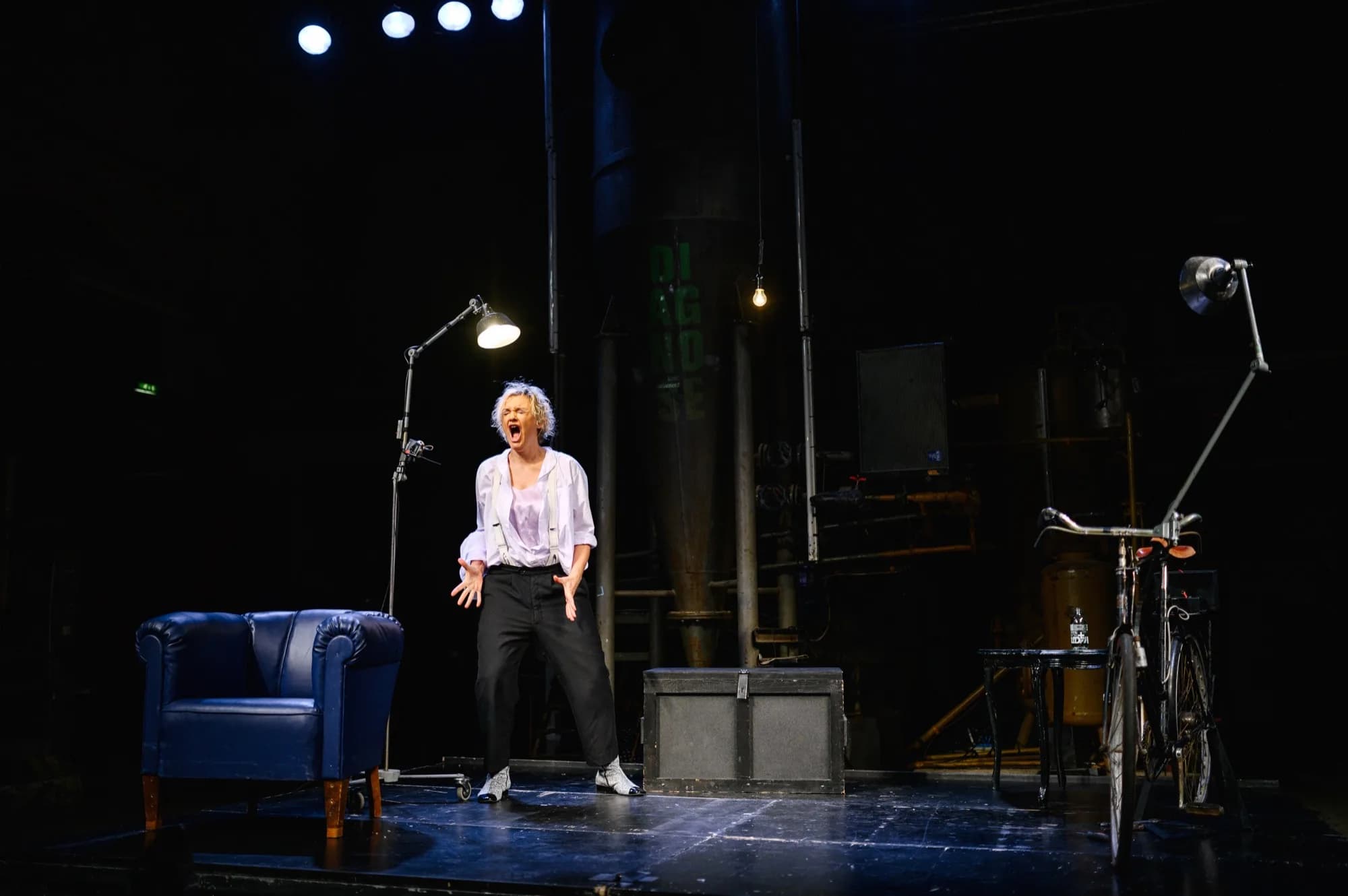 Anna Windmüller in Blackbird — schreiend auf der Bühne, blauer Sessel und Fahrrad in der Kulisse