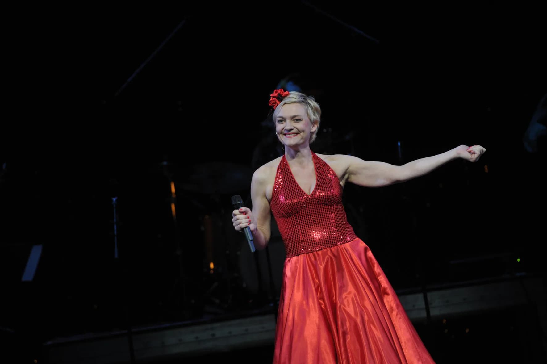 Anna Windmüller in rotem Glitzerkleid mit Mikrofon auf der Bühne, freundliche Geste, Galashow — Wendepunkt zwischen Krise und Befreiung