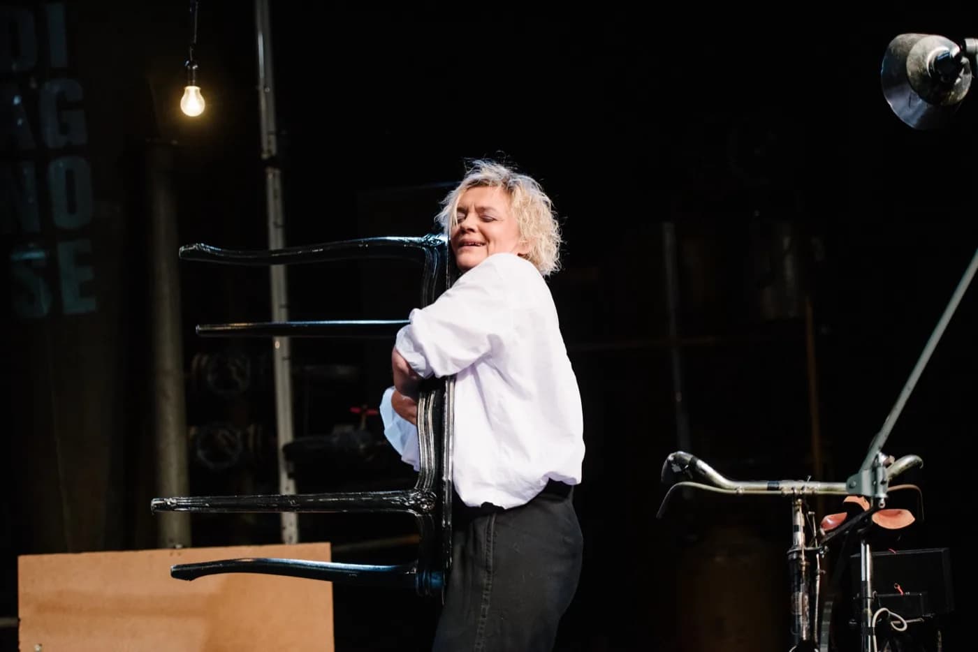 Anna Windmüller in Blackbird — einen Holzstuhl umarmend, weißes Hemd